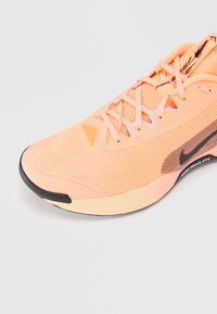 Chaussure de trail Nike en orange pastel, avec une tige en mesh texturé, des lacets plats et une semelle en caoutchouc noir avec des accents de design subtils.
