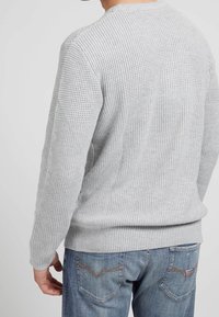 Pull en tricot gris clair avec un motif texturé, doté d'un ourlet et de poignets côtelés. Associé à un jean en denim bleu.