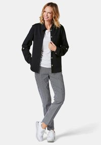 Schwarze Knopfjacket über einem weißen Oberteil, kombiniert mit schwarz-weißen karierten Hosen und weißen Sneakers. Merkmale sind Taschen und Knopfdetails.