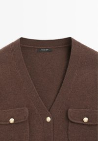 Brązowy dziany kardigan z dekoltem w serek, z dwoma kieszeniami na piersi i złotymi akcentami w postaci guzików. Miękka tekstura, zaprojektowany z myślą o komforcie i stylu.