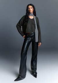 Pulover scurt de culoare gri închis, pantaloni evazați negri din piele și o eșarfă cu dungi alb-negru, având o textură fină și pantofi ascuțiți.