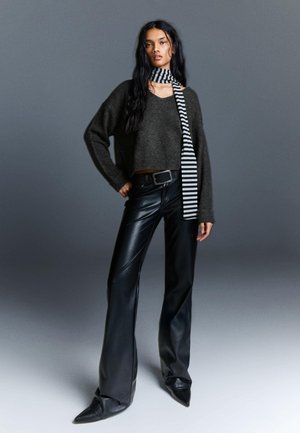 Sötétszürke cropped pulóver, fekete bőr flared nadrág és egy fekete-fehér csíkos sál, sima textúrával és hegyes orrú cipőkkel.