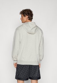 Lys grå hættepullover med en afslappet pasform, der har en kengurulomme og ribbede manchetter, parret med mønstret sorte shorts.