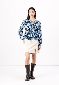 Kvetinová blúzka s peplum strihom na čiernom pozadí, modré kvety a detail na šnúrku. V páre s béžovou kordurovou sukňou s predným rozparkem.