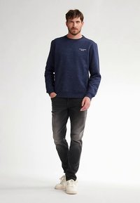 Laivastonsininen collegepaita pilkullisella kuviolla, pyöreällä pääntiellä, resoroiduilla hihansuuilla ja helmalla; yhdistetty haalistuneisiin mustiin farkkuihin ja valkoisiin lenkkareihin.