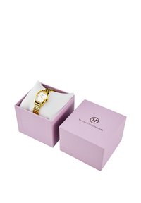 Goldene Armbanduhr mit einem weißen Zifferblatt und einem Metallband, präsentiert auf einem weichen weißen Kissen in einer helllila Box.