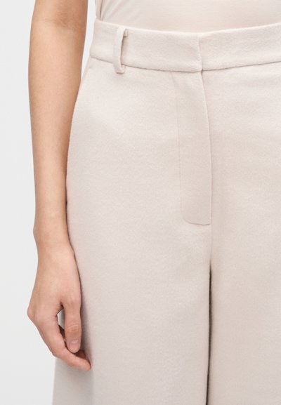 Pantaloni largi bej deschis, croială ținută, confecționați dintr-un material moale și texturat, cu buzunar lateral și talie plată cu bucle pentru curea.