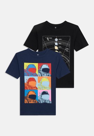 Δύο κοντομάνικα μπλουζάκια με θέμα το διάστημα· ένα μπλε σκούρο με έξι πολύχρωμες απεικονίσεις κράνων αστροναυτών, ένα μαύρο με διάγραμμα του ηλιακού συστήματος και διαστημικά σκάφη.