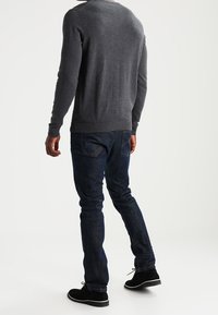 Grå stickad tröja, mörkblå jeans och svarta avslappnade skor; enkel design, figurformad och slät textur med minimal detaljering.