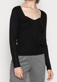Svart ribbad långärmad tröja med fyrkantig halsringning och texturerade detaljer, i kombination med rutiga byxor.