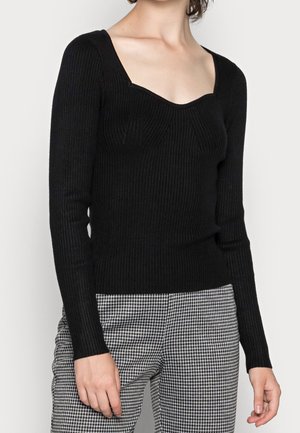 Black ribbed long-sleeve sweater with a square neckline and textured detailing, paired with checkered trousers.
