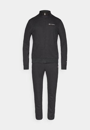 Survêtement noir en mélange de coton doux ; comprend une veste zippée avec col montant et un pantalon assorti à coupe fuselée. Logo visible sur la veste.