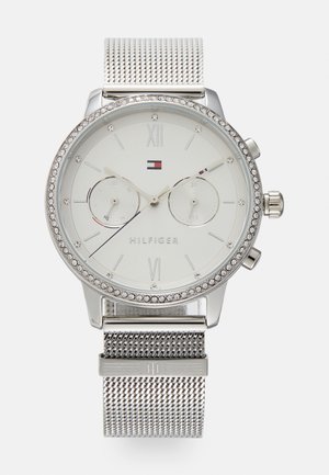 Montre-bracelet Tommy Hilfiger argentée avec bracelet en maille, lunette ornée de cristaux, double sous-cadrans, et cadran blanc minimaliste affichant l'heure et la date.