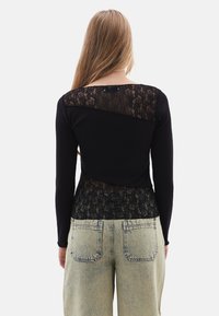 Schwarzes Langarmoberteil mit einem Spitzenrücken und einer figurbetonten Passform, kombiniert mit locker sitzenden hellblauen Jeans.