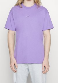 Paarse katoenen T-shirt met korte mouwen, ronde hals en klein wit Nike-logo op de borst. Klassieke relaxte pasvorm, gladde textuur.