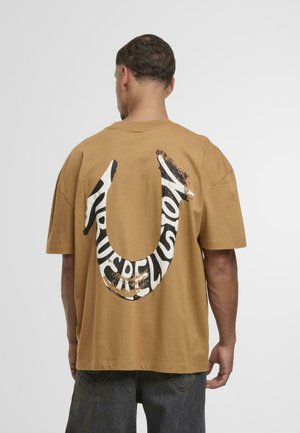 Bruine katoenen t-shirt met een groot zwart-wit grafisch ontwerp met de tekst "TRUE RELIGION" in een gebogen design op de achterkant. Losse pasvorm en korte mouwen.