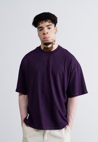 Lilla oversized t-shirt med korte ærmer, rund halsudskæring og glat tekstur. Bærert med cremefarvede bukser, der har en afslappet stil.