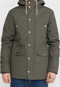 Olivgrön isolerad jacka med huva, knappknäppning fram, två bröstfickor och elastiska ärmslut; har kontrasterande bruna läderdetaljer.