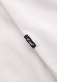 Producto de tela blanca con una etiqueta negra que dice "LEVEL UP". Textura suave, diseño sencillo y costuras visibles.