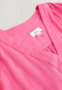 Rozā lina tops ar V-veida izgriezumu, krokojumu pie krūtīm un pie kakla piešūtu etiķeti ar uzrakstu "next". Gluda tekstūra.