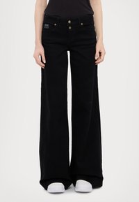 Black wide-leg jeans made of denim, featuring a high waist, gold button accents, and a relaxed fit through the legs. Pairing with white shoes.