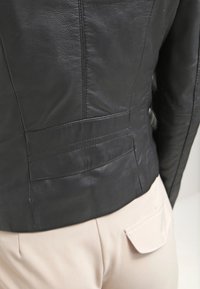 Svart läderjacka med en åtsittande design, med sömdetaljer och en diskret bakficka. Slät textur med minimalt av hårdvara.