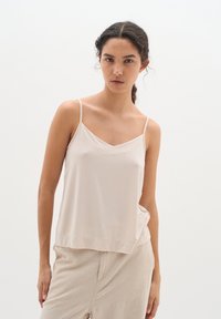 Top in cammello chiaro con spalline sottili, scollatura a V, un fit morbido e tessuto morbido, abbinato a pantaloni beige chiaro per un look coordinato.