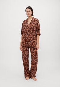 Leopardprint pyjamapakket in bruin en zwart, met een korte mouwen button-up top en lange, losse broek met een gladde textuur.