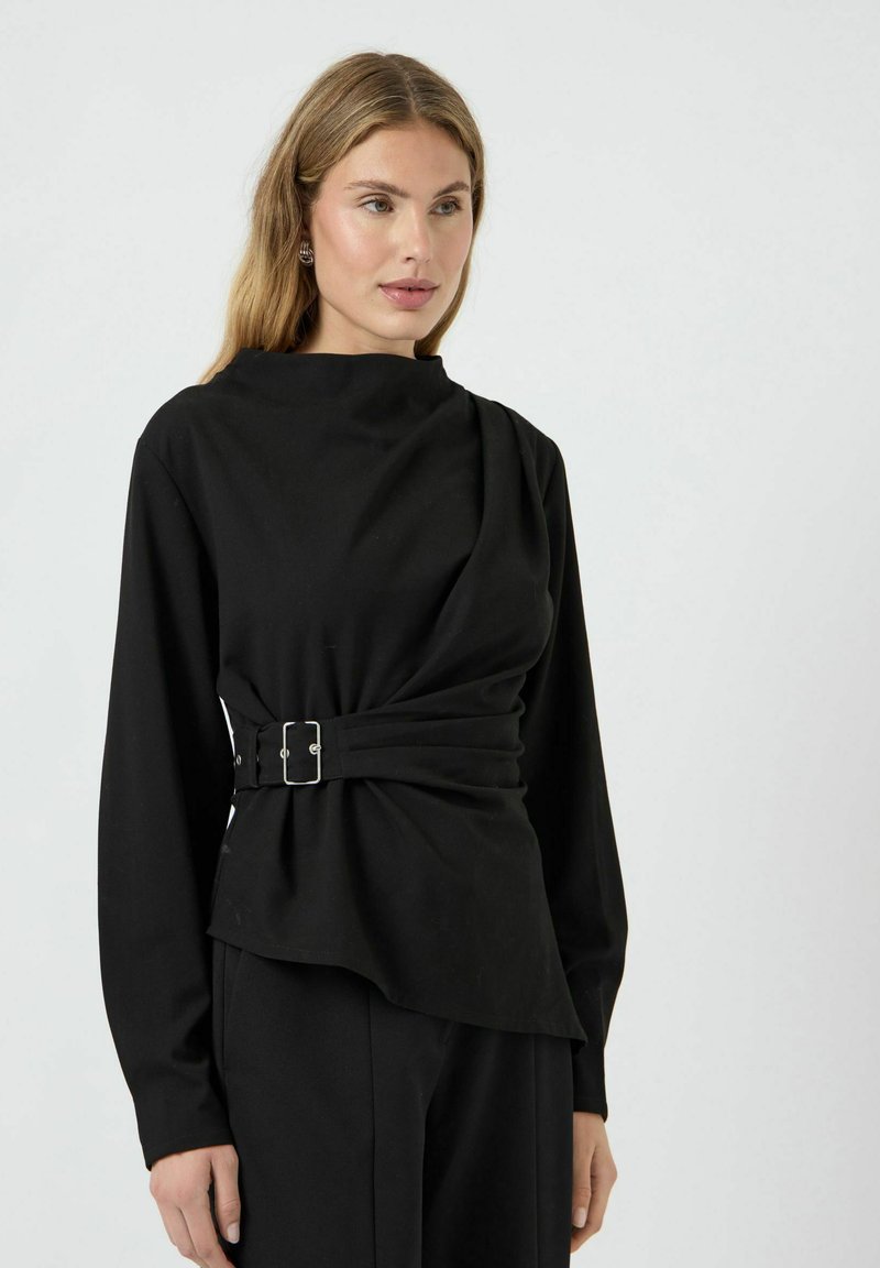 Top noir à manches longues, présentant un décolleté structuré et un détail de boucle sur le côté ; fabriqué en tissu lisse et léger.