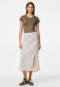 Brun tajt kortärmad topp tillsammans med en vit blommig mönstrad kjol med en sidoflik, bärs med bruna sneakers.