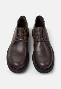 Zapatos de cuero marrón con una textura suave, puntas redondeadas y un diseño minimalista. Presentan suelas de goma negras y cordones a juego.