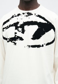 Φούτερ με στρογγυλή λαιμόκοψη σε εκρού χρώμα με ένα μεγάλο μαύρο αφηρημένο σχέδιο, κατασκευασμένο από μαλακό βαμβάκι, με ριμπ μανσέτες και τελείωμα για άνετη εφαρμογή.