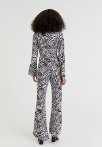 Zwart-witte zebra-print jumpsuit met lange klokmouwen en uitlopende broekspijpen, gemaakt van een soepele stof. De achterkant toont een aansluitende taille.