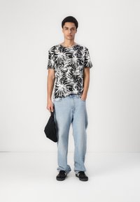 Sort-hvid kortærmet skjorte med palmebladmønster, bæret med lyseblå løse jeans og sorte sneakers, og holder en sort taske.