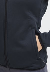Giacca softshell blu navy con zip e tasche laterali. Tessuto liscio, design aderente e polsini elasticizzati per una vestibilità aderente.