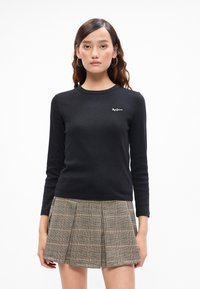 Fekete, hosszú ujjú, bordázott felső kerek nyakkal és fehér logóval a mellkason, kiegészítve egy pliszírozott, kockás miniszoknyával.