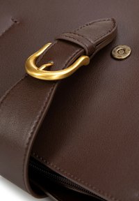 Primo piano di una borsa in pelle marrone con una fibbia in metallo dorato, superficie texturizzata e un pulsante decorativo con un motivo geometrico.