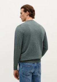 Pull en tricot vert à manches longues, col rond et ourlet côtelé, associé à un jean en denim bleu. Texture lisse et style ajusté.
