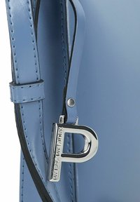 Borsa a mano in pelle blu con texture liscia, dotata di una tracolla nera e un ciondolo d'argento a forma di lettera "P" inciso con testo.