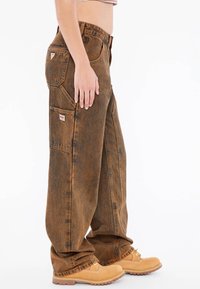 Bruine denim cargo broeken met een relaxte pasvorm, voorzien van meerdere zakken en een vervaagde textuur, gecombineerd met tan kleurige werklaarzen.