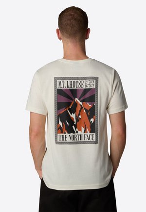 Cream-colored t-shirt featuring a graphic of Mt. Lhotse with orange and black mountains, rays emanating from the peak, and "The North Face" text.