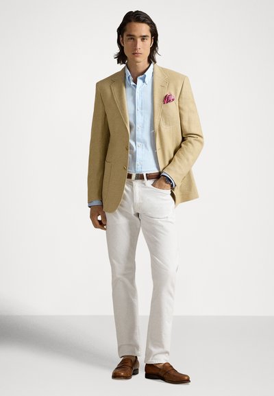 Μπεζ σακάκι, γαλάζιο και λευκό ριγέ πουκάμισο, λευκό παντελόνι, καφέ παπούτσια. Μαντήλι στην τσέπη προσθέτει μια πινελιά χρώματος. Απλός, ραμμένος σχεδιασμός.