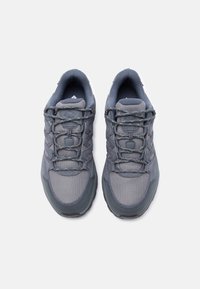 Ζευγάρι γκρι αθλητικά παπούτσια με λεπτομέρειες από δίχτυ και σουέντ, ανακλαστικά κορδόνια και επενδυμένους γιακάδες, απεικονίζεται από επάνω σε λευκό φόντο.