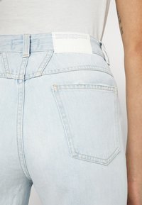 Ljusblå denimjeans bärs tillsammans med en vit skjorta, med bakfickan och det märkta lapparna på midjebandet synliga.