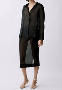 Schwarze transparente Bluse mit langen Ärmeln und durchgehender Knopfleiste, kombiniert mit einem passenden transparenten Rock, der unterhalb des Knies endet. Minimalistisches Design.