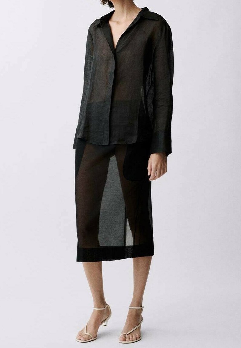 Schwarze transparente Bluse mit langen Ärmeln und durchgehender Knopfleiste, kombiniert mit einem passenden transparenten Rock, der unterhalb des Knies endet. Minimalistisches Design.