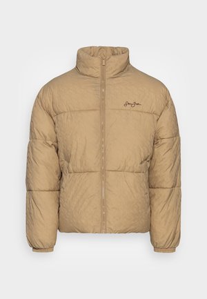Doudoune beige avec un col montant, texture matelassée, fermeture éclair sur le devant et logo brodé sur la poitrine gauche.