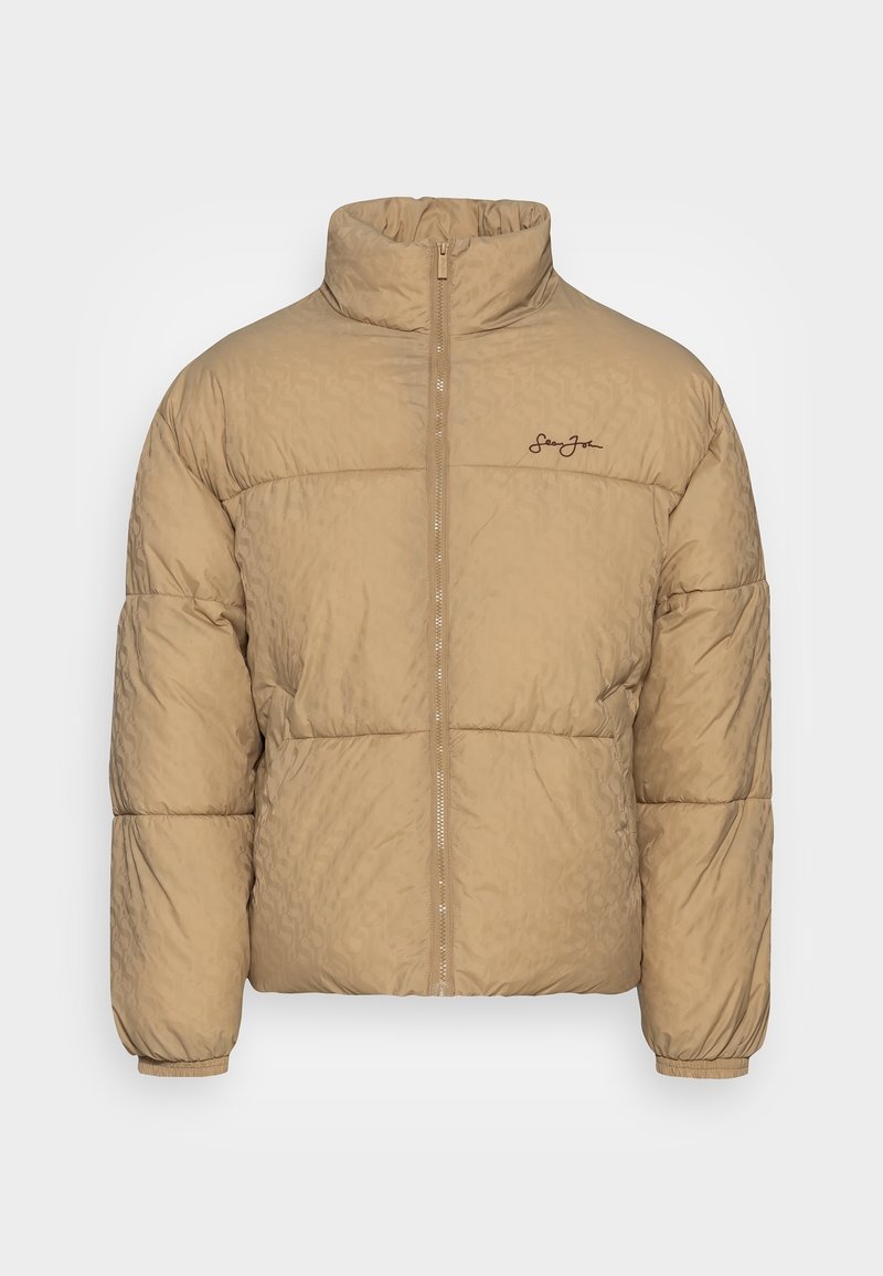Doudoune beige avec un col montant, texture matelassée, fermeture éclair sur le devant et logo brodé sur la poitrine gauche.