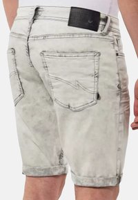 Shorts en denim gris clair avec ourlets retournés, dotés de deux poches arrière à patch et d'une ceinture noire avec perforations. Design minimaliste.