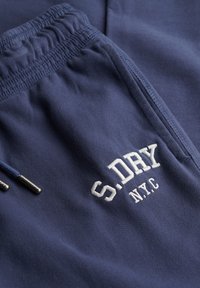 Granatowe spodnie dresowe z elastycznym pasem. Posiadają biały, haftowany logo "S.DRY NYC". Gładka faktura z metalowymi akcentami na sznurku.